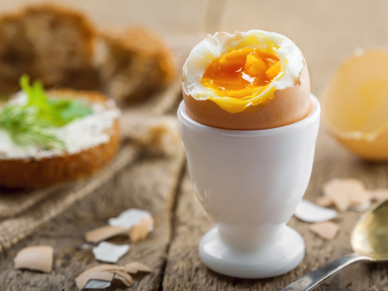 A boiled agg in a white egg cup with the top cut off and the yolk visible, on a wooden table.