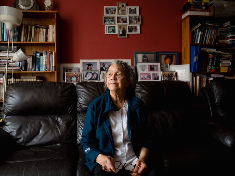 Marion Blake from Luton sits looking thoughtfully on the sofa in her living room in front of photographs of her family.
