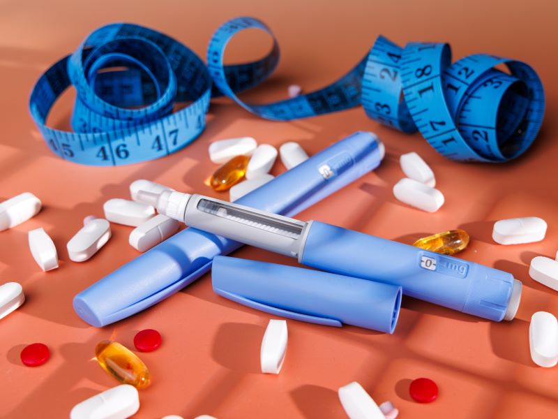 Weight-loss injection pens and pills on a table with a tape measure.