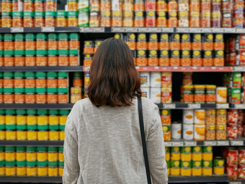 A woman looking at tins of baked beans on shelves in a supermarket.