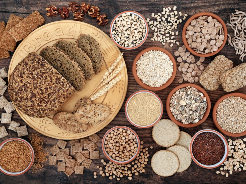 Wholegrain foods, including wholemeal bread, brown rice and wholegrain cereals, on a table.