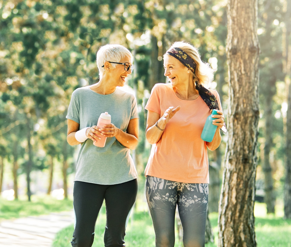 Two older women wearing exercise clothes, walking with water bottles, smiling and chatting.