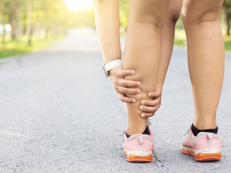 A woman walking outside holding onto her calf in pain.