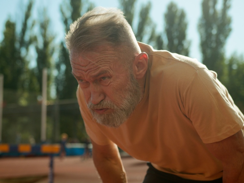 A man feeling breathless outside with his hands on his legs.