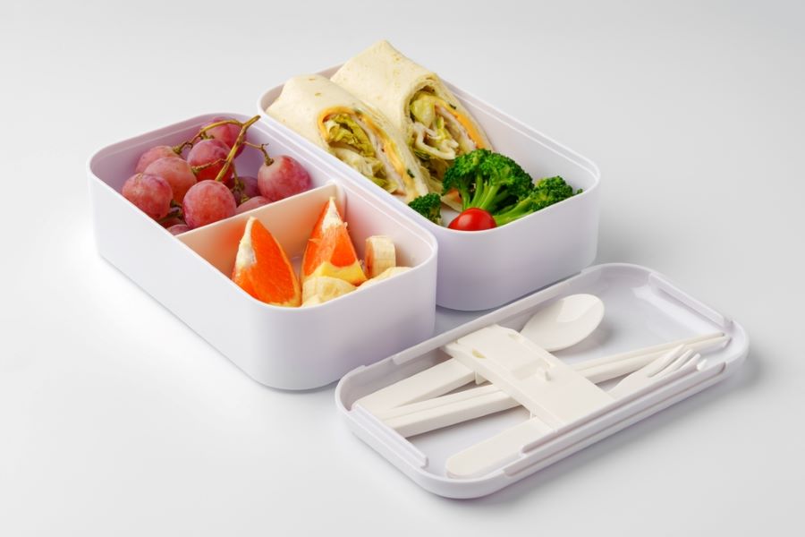 Open lunch box with grapes, orange slices, broccoli and sandwich wrap