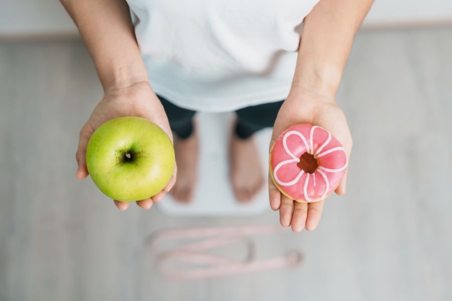Person standing on a scale holding a green apple and iced doughnut