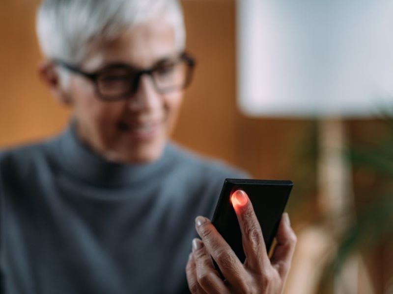 Close up of a senior woman with short hair and glasses holding her finger against the light on the back of her mobile phone
