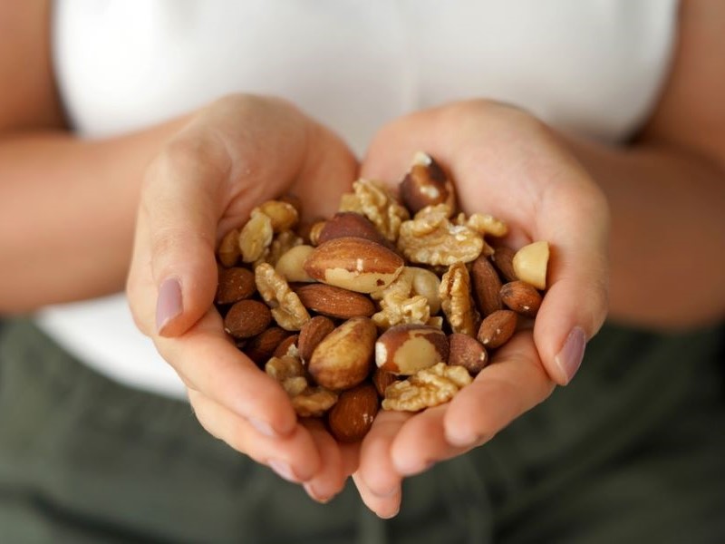 A white woman's hands are holding a selection of different nuts. She is wearing a white top.