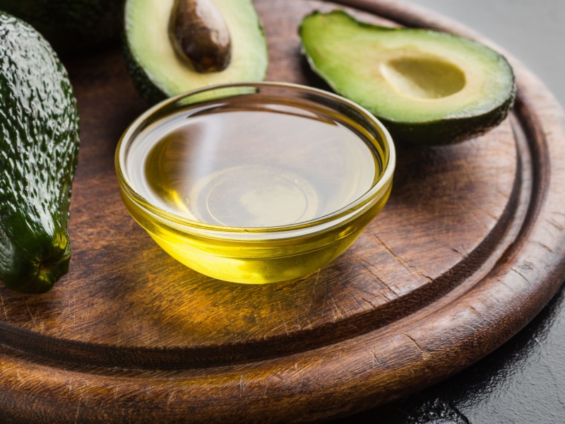 A bowl of avocado oil next to halved avocados.