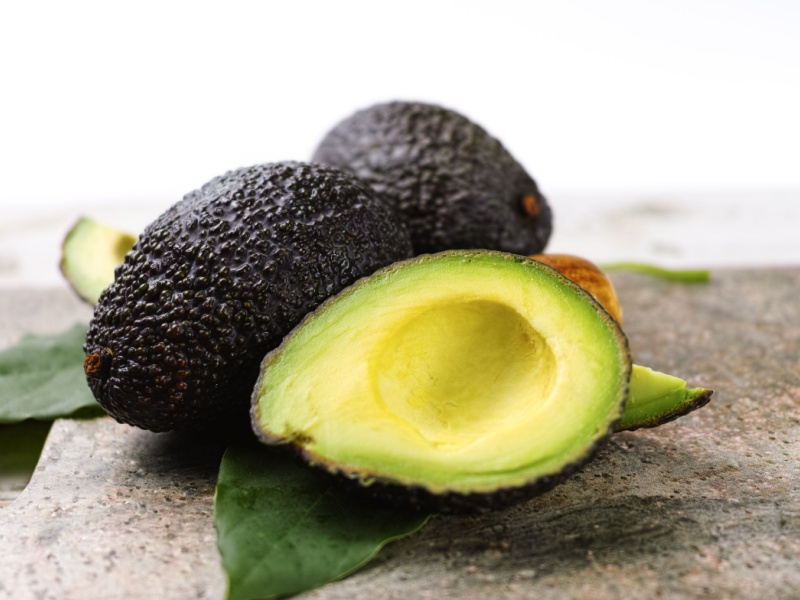 Half an avocado next to whole avocados on a table.