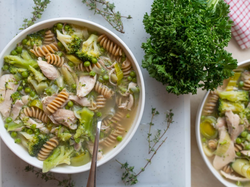 A white bowl filled with fusilli pasta, chicken, greens and broth.