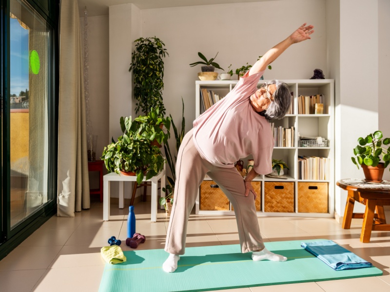 A woman at home stretching her arm up and over her head.