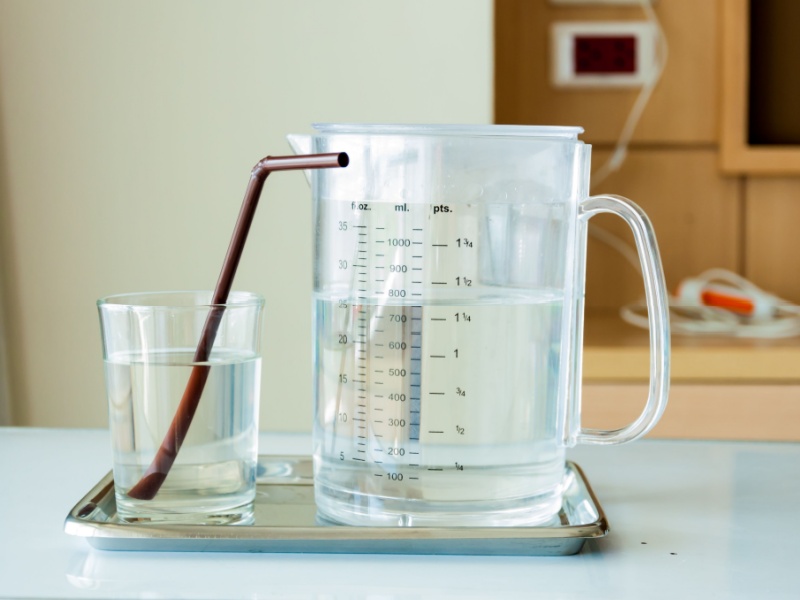 A jug of water and a glass with a straw in a hospital.