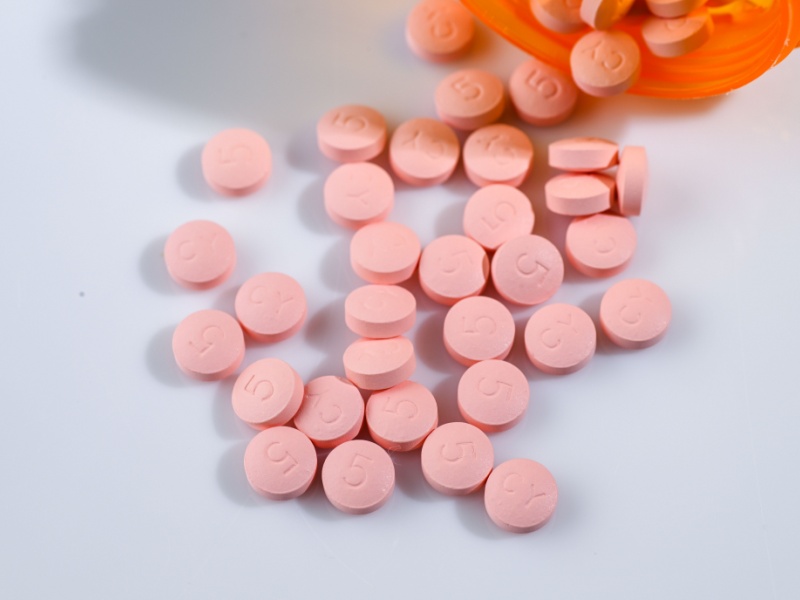 Pink statin pills spilling out of a bottle onto a table.