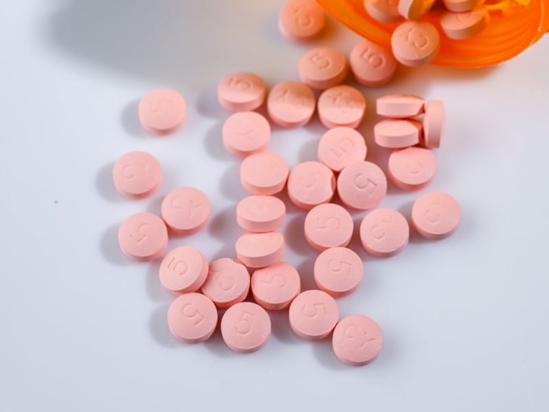 Pink statin pills spilling out of a bottle onto a table.