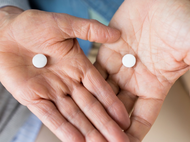 Hands holding 2 identical statin pills.