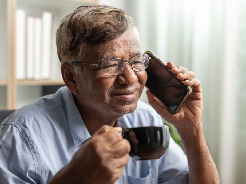 A man drinking a hot drink while chatting on the phone.