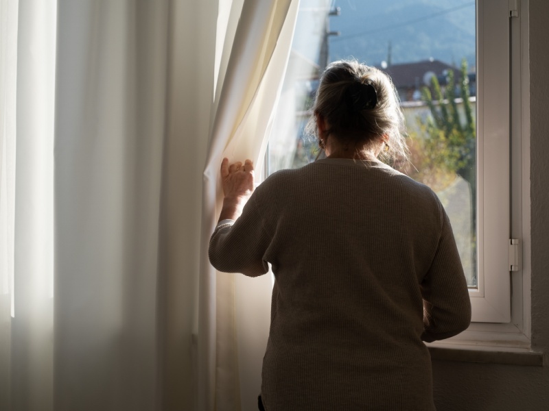 A woman at home looking out of her window.