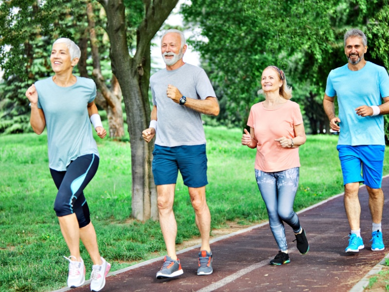 A group of seniors in sports clothing running on a track in a park with trees in the background