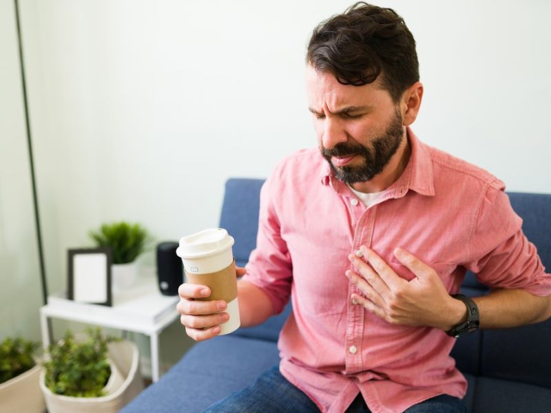 A man holding a cup of coffee while touching his chest.