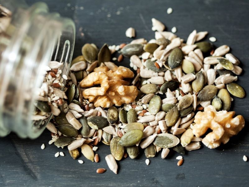 A jar of nuts and seeds spilling on to a table.