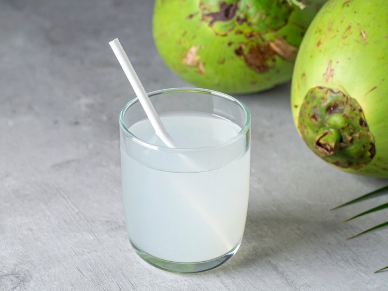 A glass of coconut water next to green coconuts.