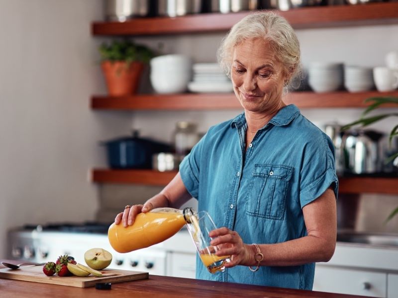 A woman pouring a glass of juice in a kitchen.