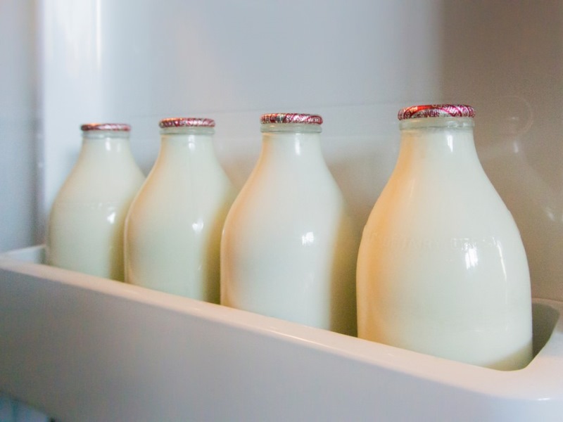 Bottles of milk on a shelf in a fridge.