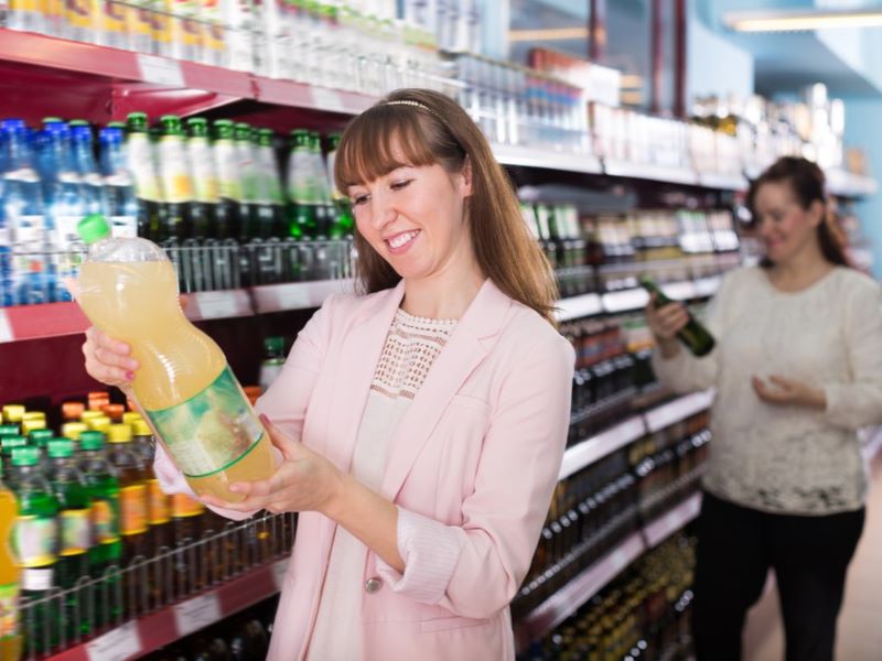 A woman holding up a bottle of squash in a supermarket.