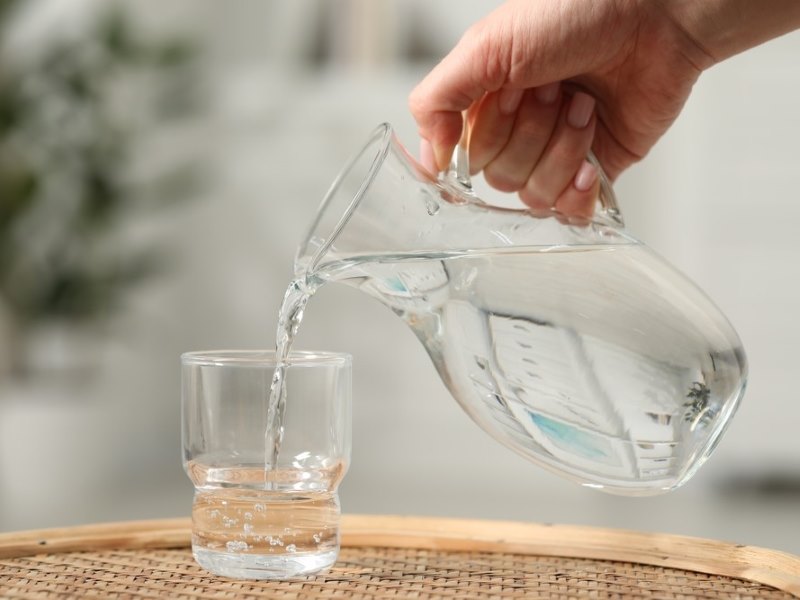 A person pouring a jug of tap water into a glass.