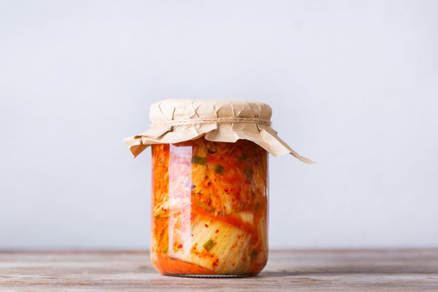 Homemade kimchi in a glass jar on a wooden table.