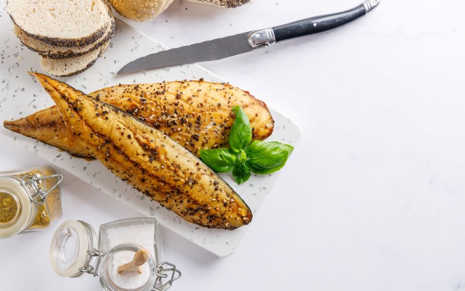 Seasoned smoked mackerel on the side on a white table top.