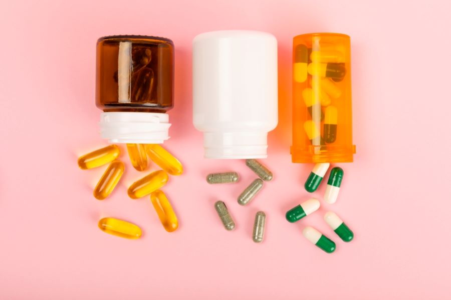 Variety of vitamins and supplements in jars on a pink background