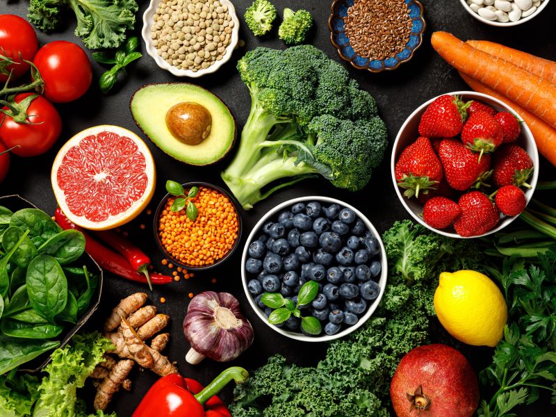 Top view of a variety of brightly coloured fruits and vegetables including blueberries, strawberries, lemon, grapefruit, broccoli, avocado, carrots and tomatoes.
