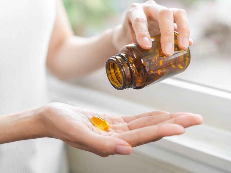 Close up of a person holding a brown bottle of supplements in one hand, holding a few of the supplement capsules in the other hand.