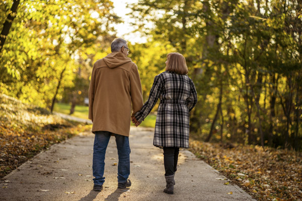 A middle-aged male and female walking along a path in an autumnal park