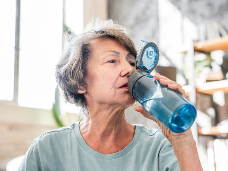 A woman drinking an electrolyte drink out of a reusable water bottle.