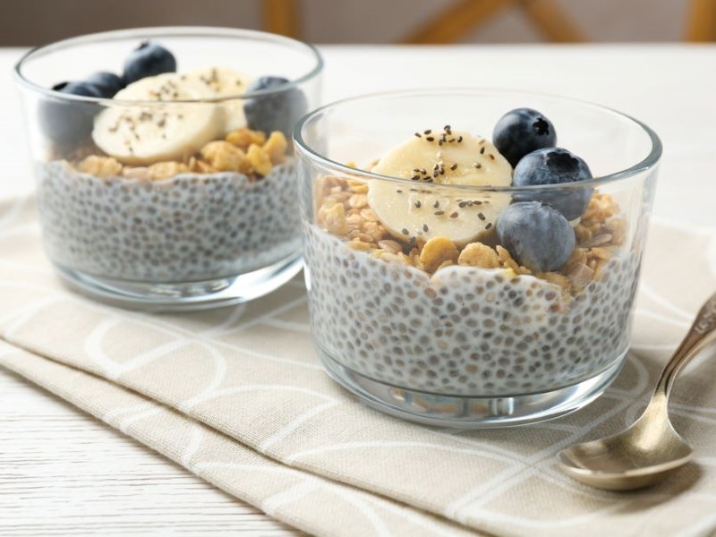 Two glass dessert bowls containing chia pudding with a topping of granola, banana and blueberries.