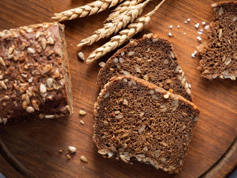 Loaf of brown seeded bread on a wooden board, next to slices.