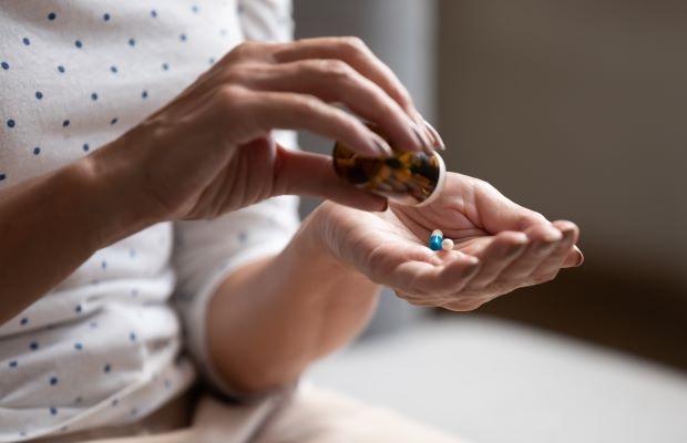 Close up of person putting medication into their hand from a pill bottle.