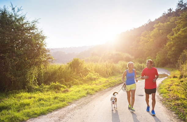 Older couple run outdoors with dog on a sunny day