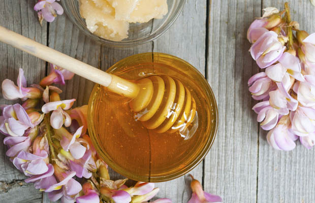 A jar of acacia honey on a wooden table, next to acacia blossoms