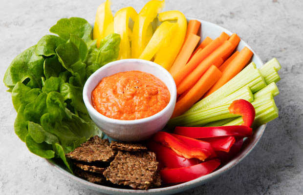 Sliced carrot, celery and mixed peppers in a bowl with a hummus dip