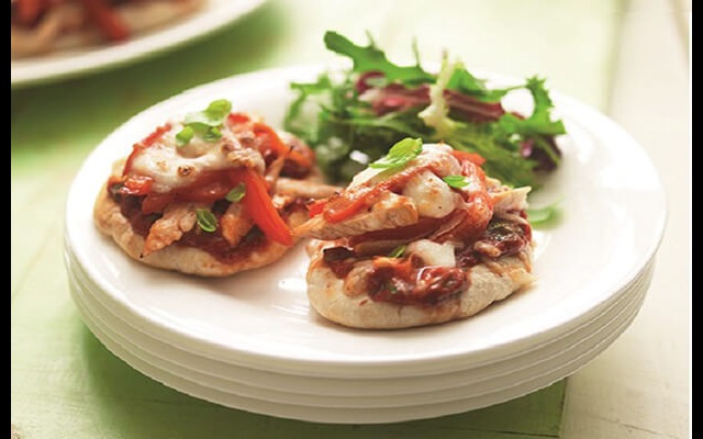 Two chicken and pepper pita pizzas on a plate with green salad on the side.