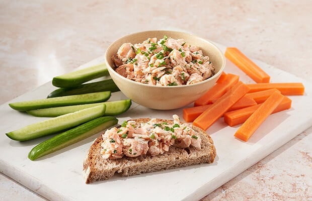Salmon pate in a bowl with chopped cucumber, carrots and a slice of wholemeal bread with the pate on top of it.