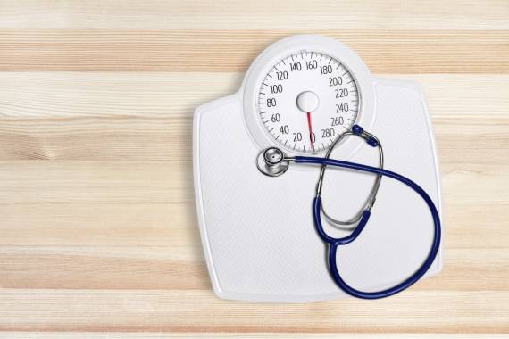 a pair of white weighing scales sitting on a wooden floor with a stethoscope resting on top of it