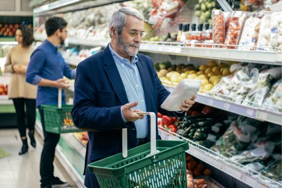 an older man in a supermarket with a basket in his hand and browsing fridges
