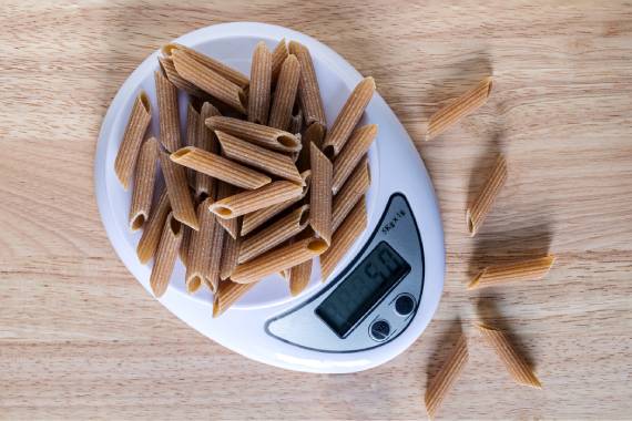 a handful of tube-shaped wholemeal pasta shells sitting on top of a white food weighing scale