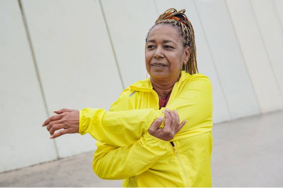 a black woman in a yellow sports jacket stretching her left arm across her body and holding her wrist with her right hand