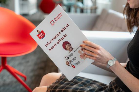 a woman sitting on a sofa holding an easy read version of the understanding a heart attack booklet